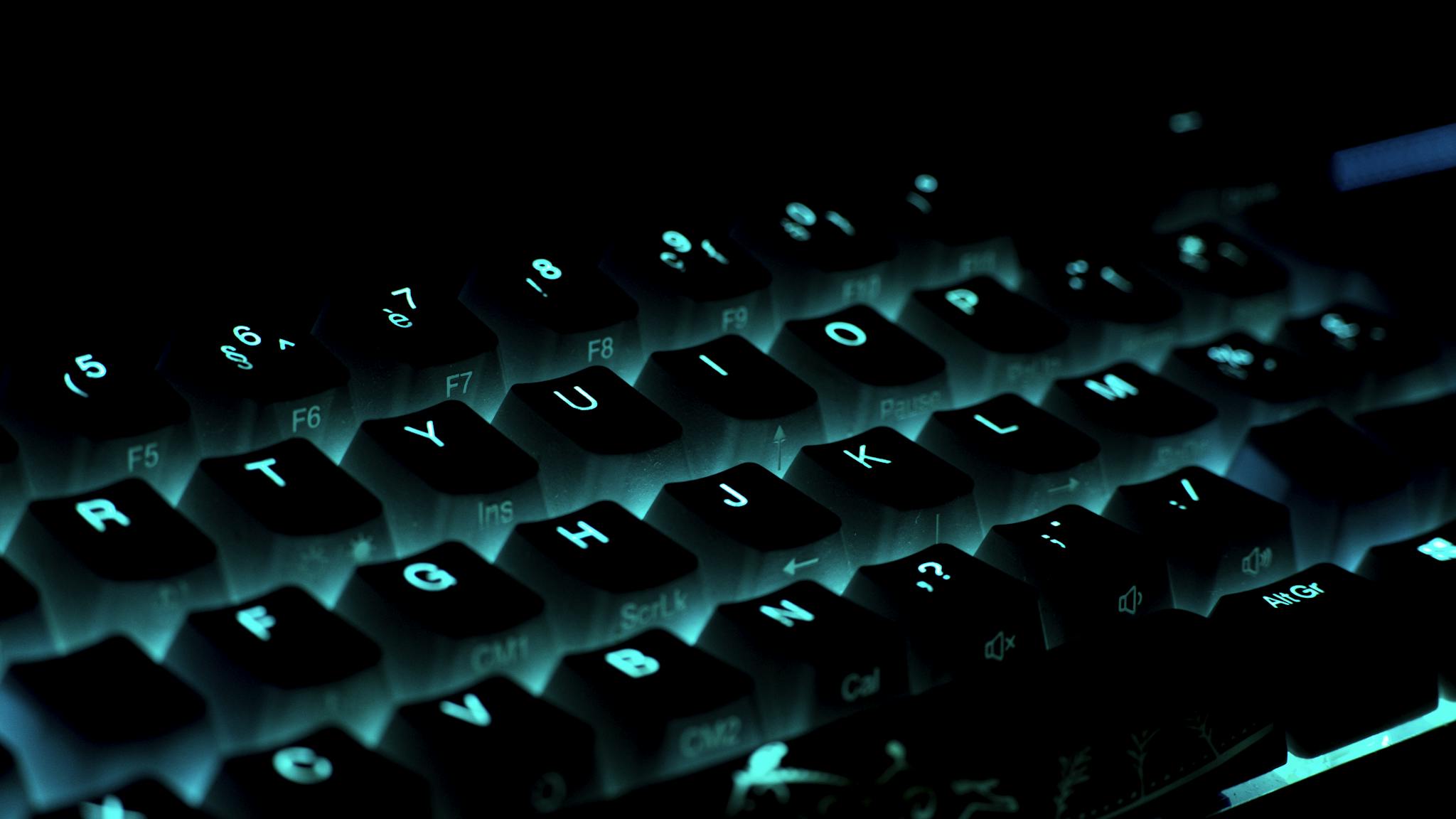 Close-up of a glowing gaming keyboard with blue backlighting in a dark ambiance.